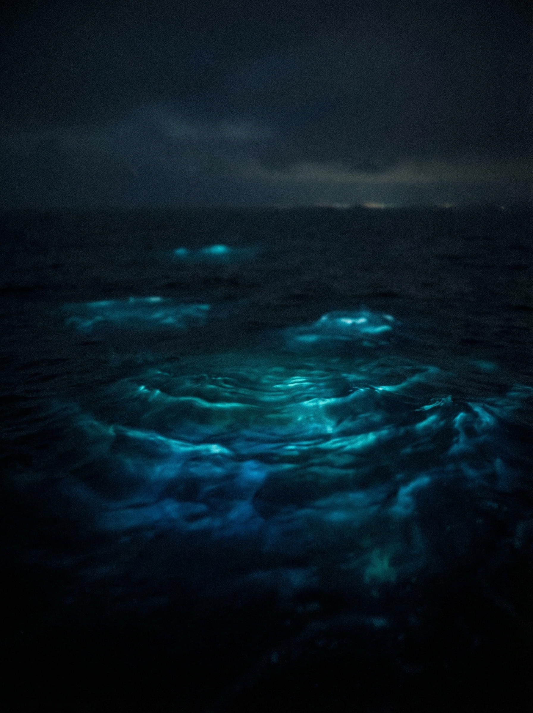 Deep dark ocean surface at night with mysterious sound waves visualized as teal bioluminescent ripples spreading across water — the unexplained sounds of the deep
